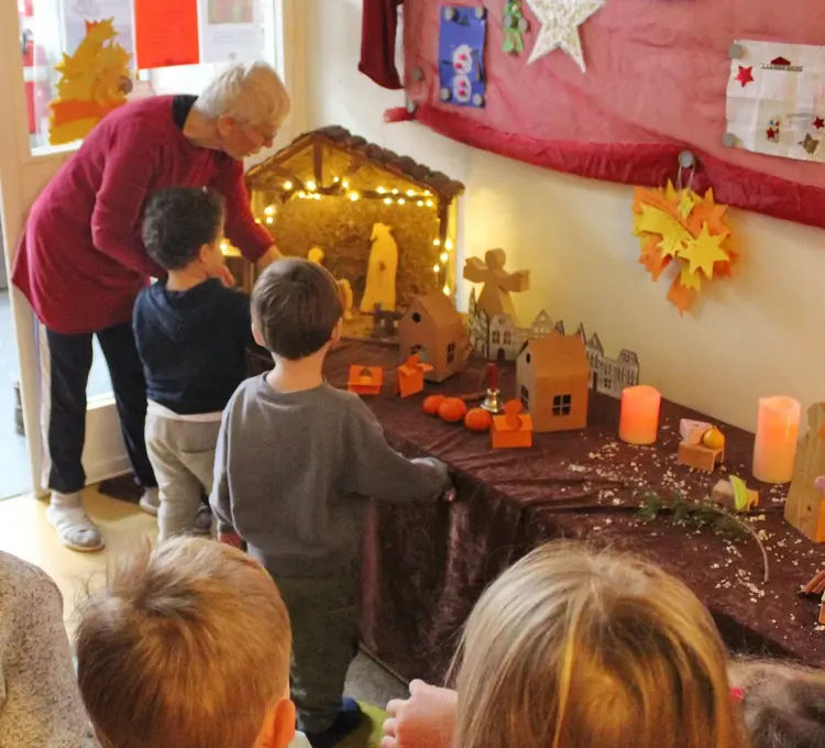 Kinder betrachten den an einem langen Tisch aufgebauten Weihnachtsweg mit Figuren, Häusern und am Ende des Weges einer Krippe